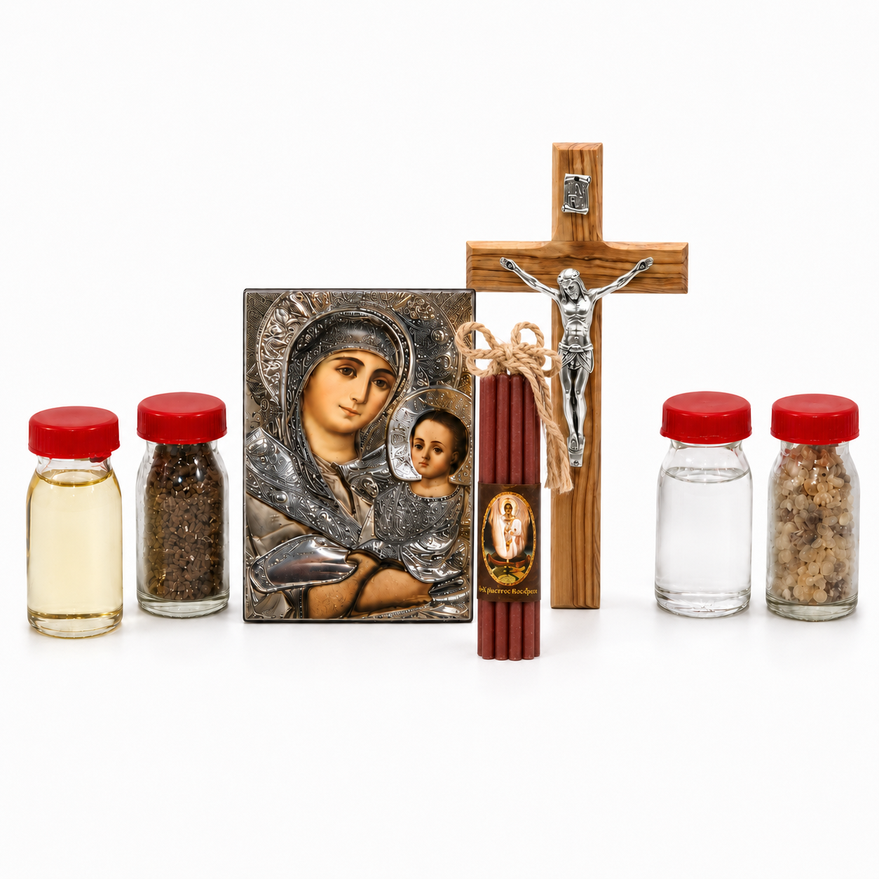 Christian home blessing set arranged on white background with Virgin Mary icon, wooden crucifix, red prayer candles tied with twine, and small glass bottles with liquid, soil and incense