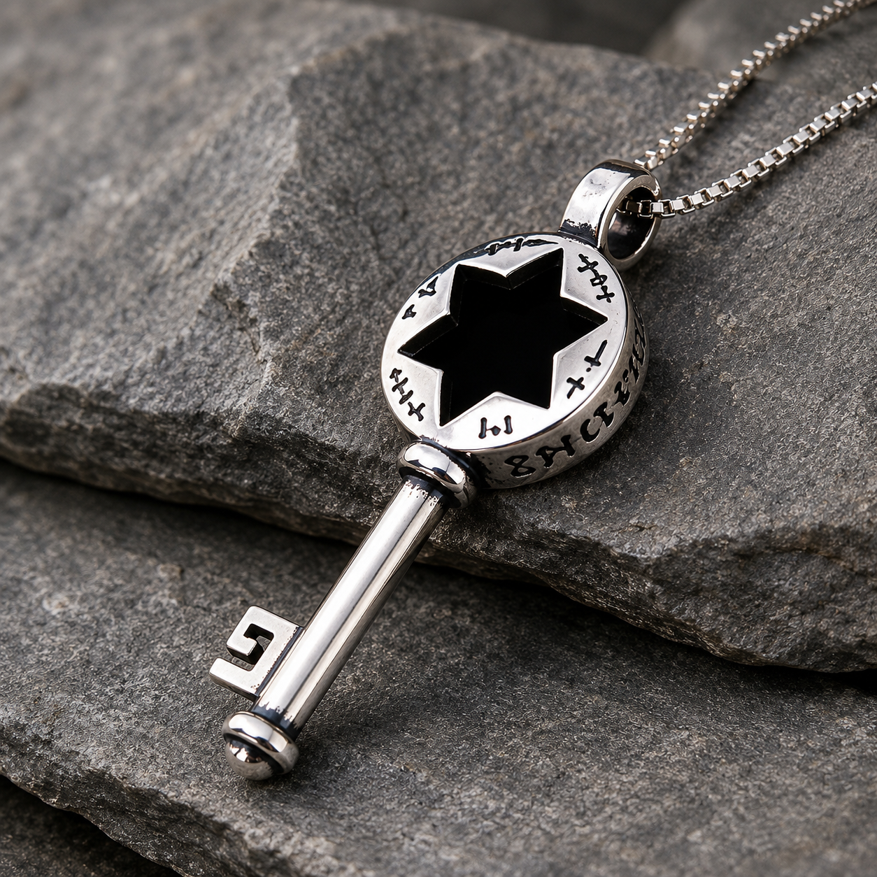 Silver-tone key pendant necklace with black six-point star cutout, Hebrew-style markings around the round top, polished metal finish, angled view on dark stacked stone background