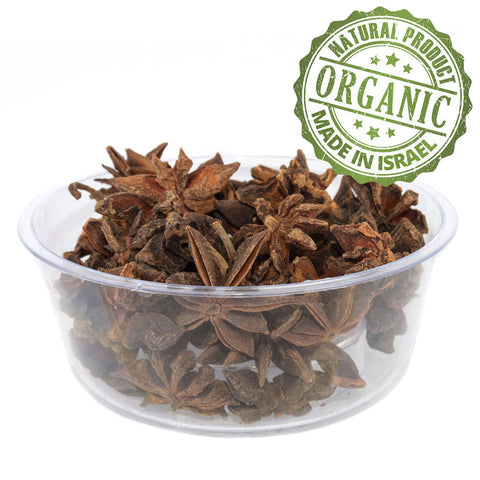 A star anise pod on a wooden spoon with other spices.
